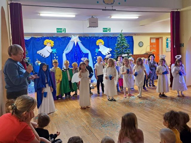 grupa dzieci w przebraniach aniołków stoi przed publicznośćią po lewej stronie kobieta z mikrofonem